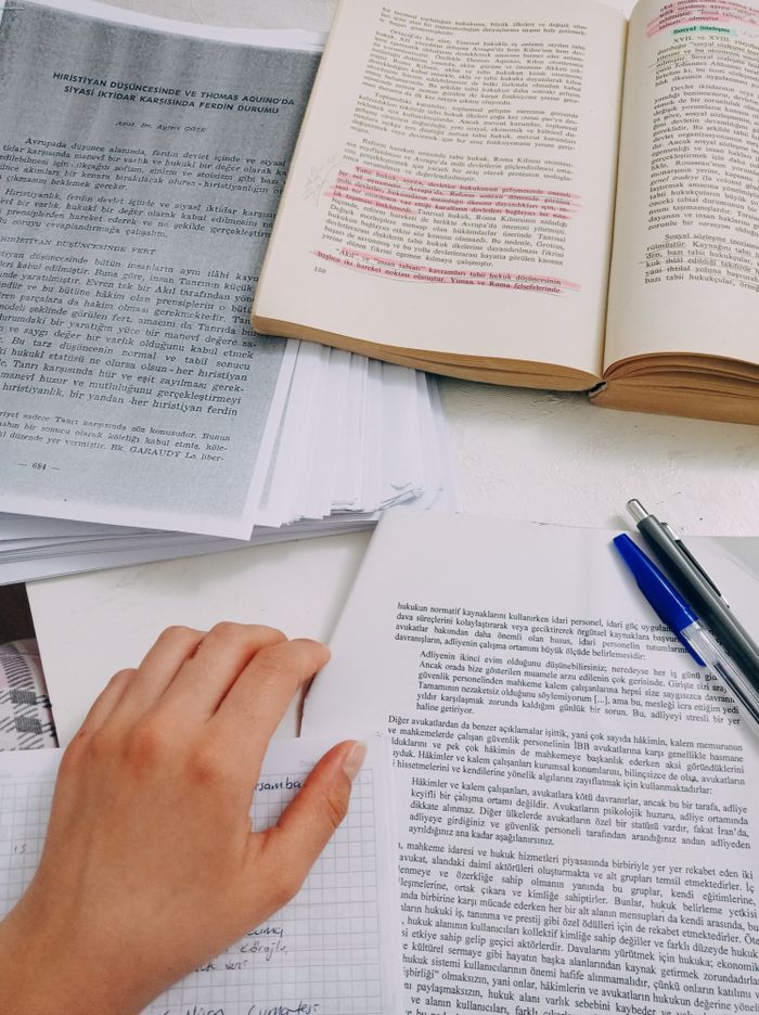 Open books and notes on a desk, featuring a hand studying, symbolizing academic focus.