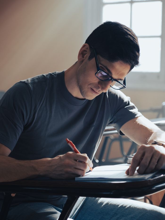 Young man focused on writing an exam in a classroom setting with natural light.